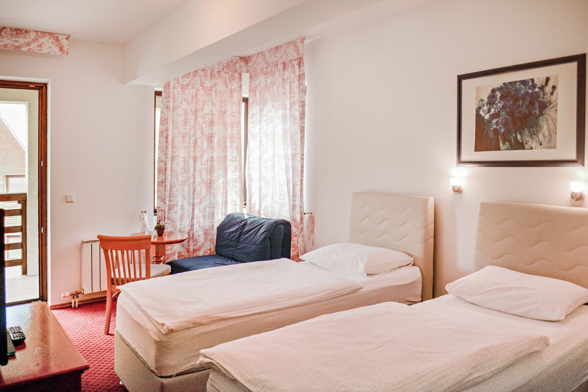 A hotel room with two beds, a desk, a chair, and a window with curtains.