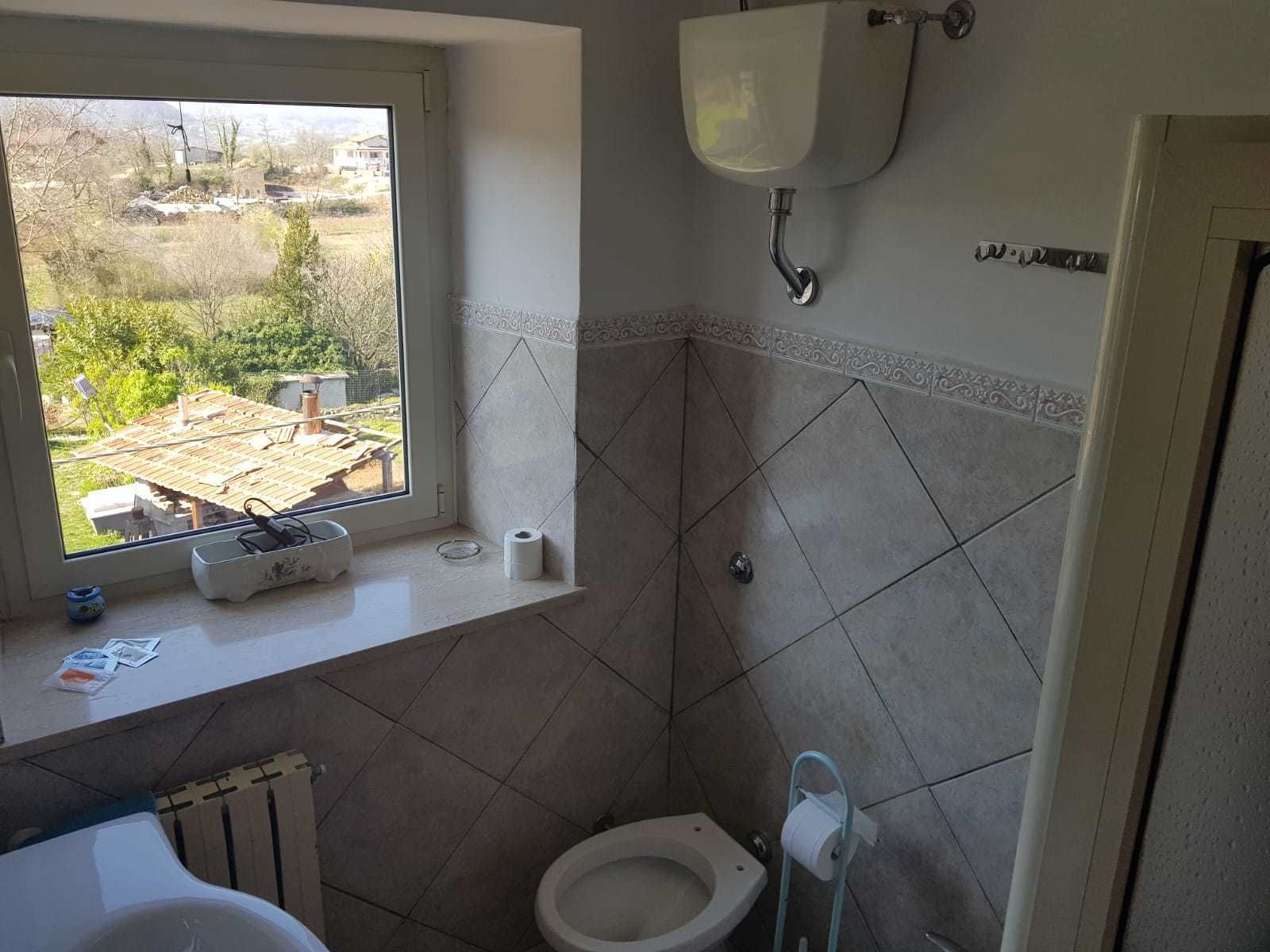 Un baño con inodoro, bidé, ventana y vista a una obra en construcción.