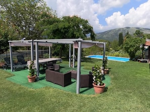 An outdoor patio with a pergola, seating, and potted plants.
