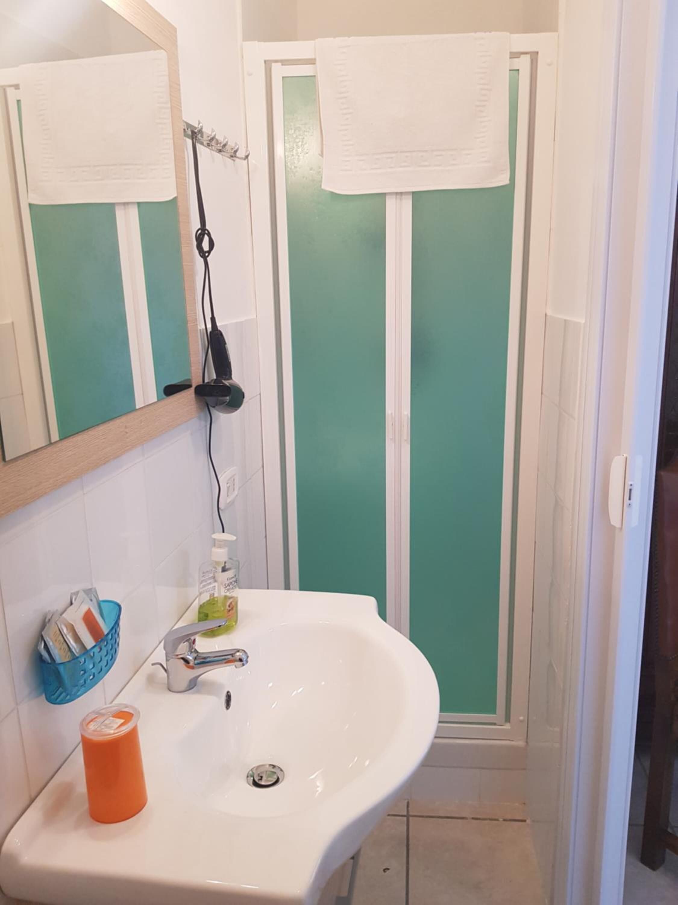 A bathroom with a white sink, a mirror, a towel hanging on the door, and a shower with frosted glass doors.