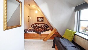 Um quarto com teto inclinado, cama com estrutura de madeira, janela com vista e espelho na parede.