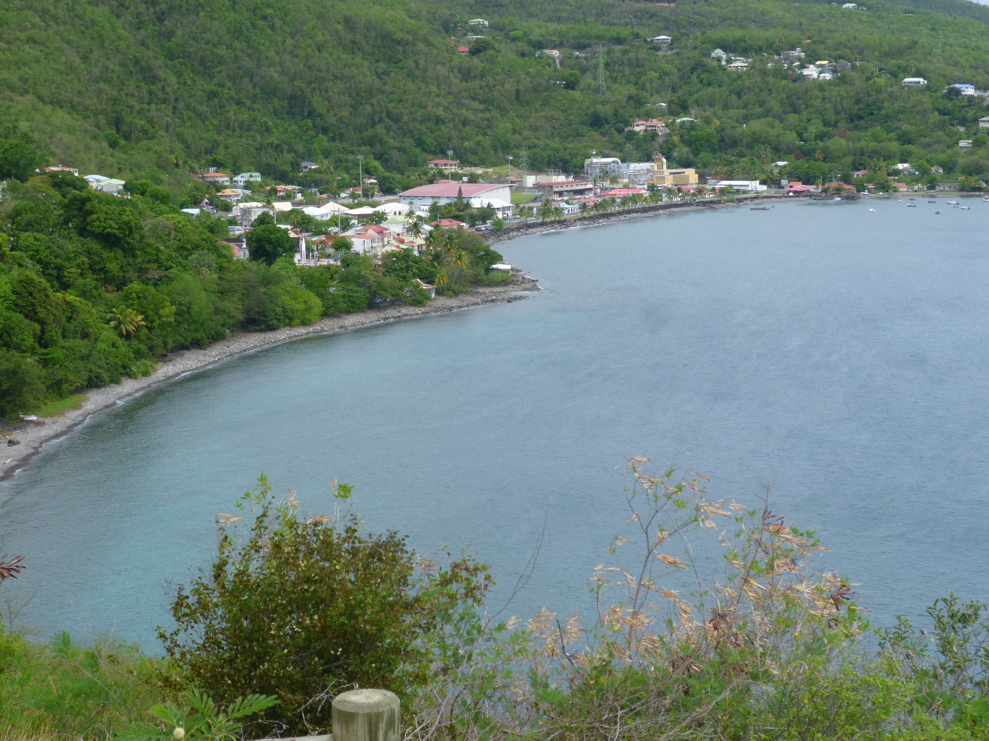 Un pueblo costero con edificios a lo largo de la costa, una vista despejada del mar y abundante vegetación al fondo.