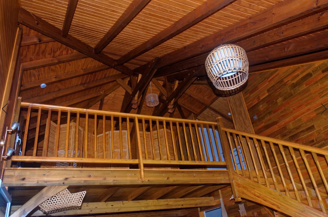 A wooden balcony with a railing, a hanging light fixture, and a wooden ceiling structure.