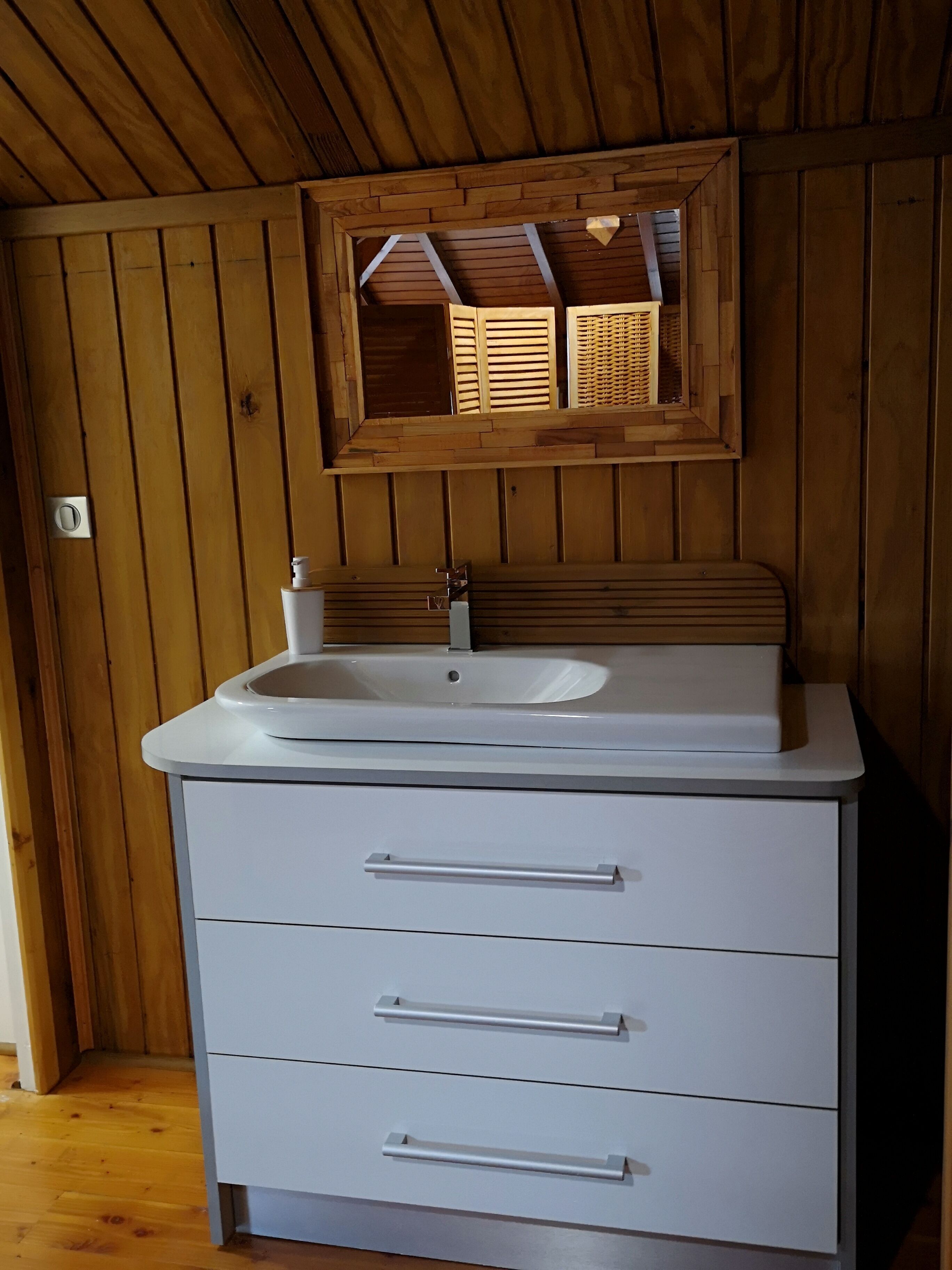 Un baño con paredes de madera, un lavamanos blanco y un espejo encima.