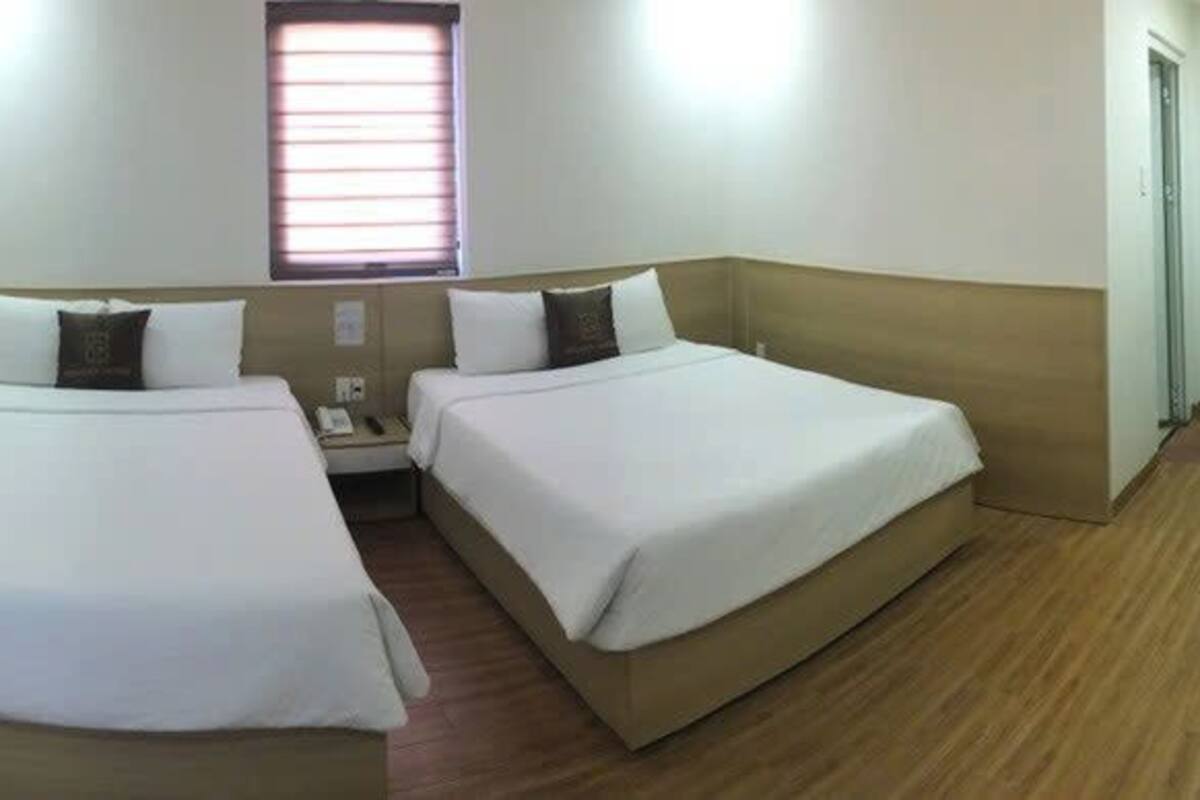 A hotel room with two beds, a desk, a mirror, a window, and a TV.