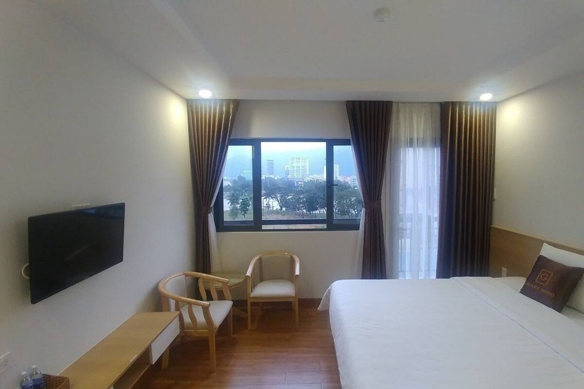 A hotel room with a bed, a TV, a chair, and a window with a city view.
