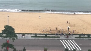 A beach with people walking and playing, a road with vehicles, and a clear view of the ocean. - Galaxy Hotel (Quy Nhon)