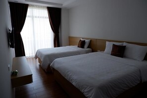 Una habitación de hotel con dos camas individuales, una mesita de noche de madera y un ventanal con cortinas.