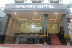 El exterior del Hotel Galaxy con una entrada despejada, una escalera que lleva a la entrada y un cartel con el nombre del hotel.