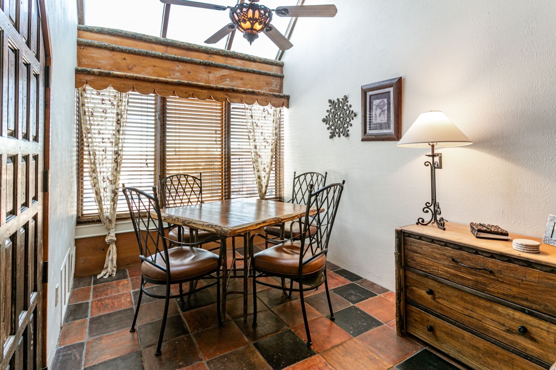 Un coin repas avec une table et des chaises en bois, un ventilateur de plafond et une lampe fixée au mur.