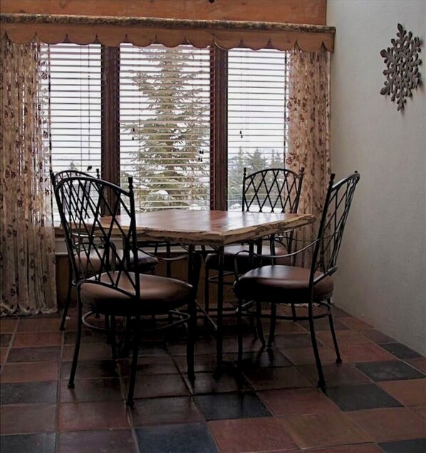 A dining area with a wooden table and four chairs, large windows with blinds, and a decorative wall piece.