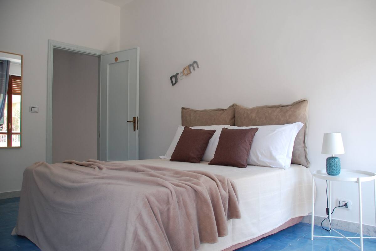 A neatly made bed with a beige blanket, a bedside lamp, and a wall-mounted sign that reads "Dream".