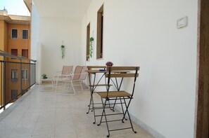 A balcony with a table and chairs, a small plant, and a window with a view of buildings. - Bari Rooms Central Station (Bari)