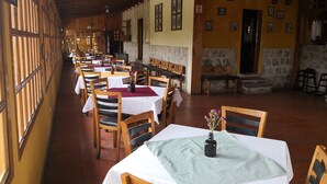 Un amplio comedor con mesas y sillas de madera, paredes de piedra y suelo de baldosas.