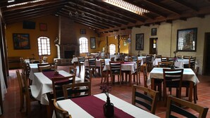 Un restaurante con varias mesas y sillas, una chimenea de ladrillo y ventanas amplias que dejan entrar luz natural.
