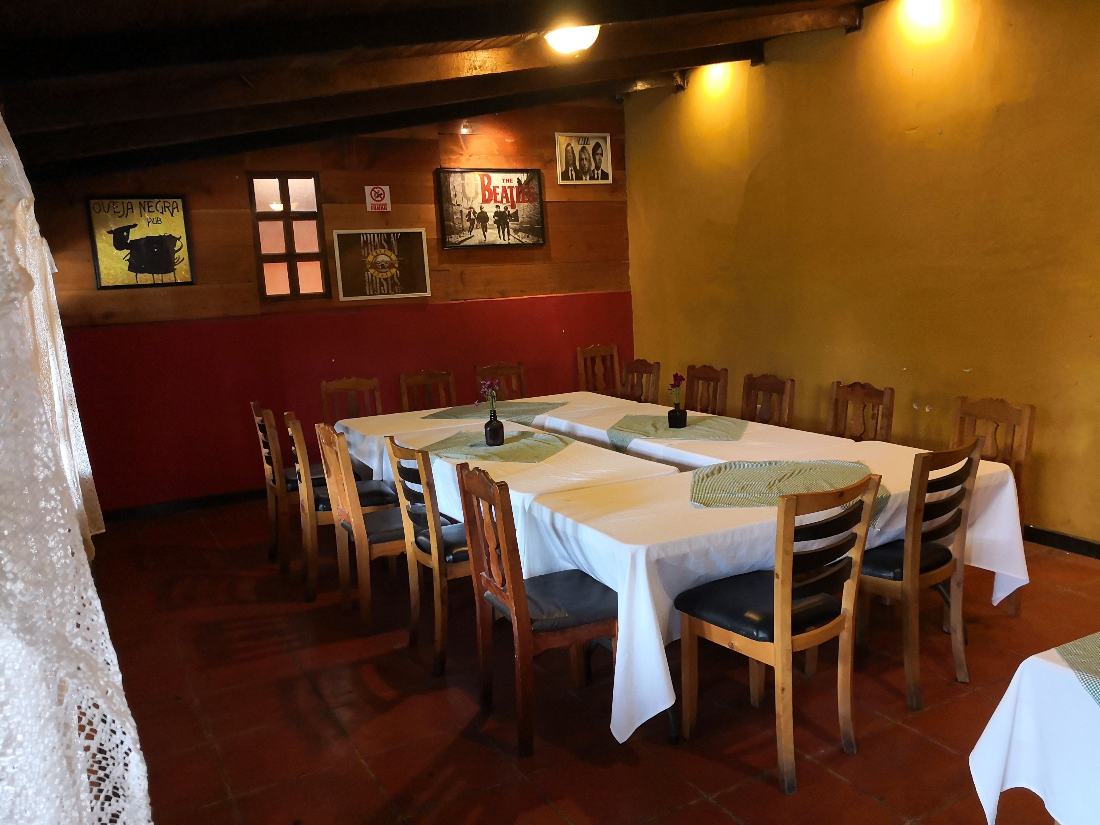 A dining area with a long table, wooden chairs, and a red wall with framed pictures.
