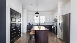A modern kitchen with a central island, dark cabinetry, stainless steel appliances, and a pendant light.