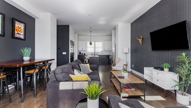 A modern living room with a sofa, coffee table, and dining area. There is a kitchen in the background with white cabinets and a black countertop.