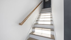 A staircase with wooden steps and a wooden handrail, leading to a dark wall with a framed map.