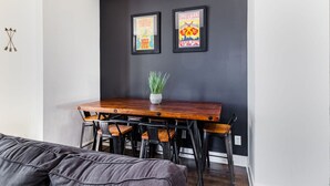 A modern room with a dark wall, a wooden dining table with four chairs, and two framed posters.