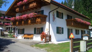 A traditional Alpine-style building with wooden balconies adorned with flowers, a bench outside, and a sign indicating a free room. - Alpspitze for 3 persons and view to the Zugspitze (Untergrainau)