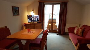 A cozy living room with a wooden dining table, red upholstered chairs, a red sofa, and a television on a wooden stand. - Alpspitze for 3 persons and view to the Zugspitze (Untergrainau)