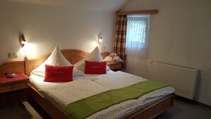 A neatly made bed with patterned bedding and two red pillows, a bedside table with a lamp, and a window with curtains. - Alpspitze for 3 persons and view to the Zugspitze (Untergrainau)