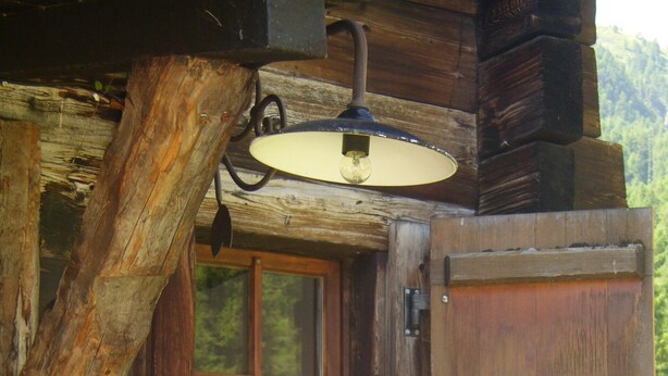 A rustic wooden cabin with a window, a door, and a hanging light fixture. - Apartment in Täsch / Zermatt for two persons (Täsch)