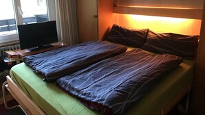 A hotel room with a bed, a television on a wooden table, and a window with curtains. - Apartment in Täsch / Zermatt for two persons (Täsch)