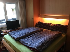 Ein Hotelzimmer mit Bett, Fernseher auf einem Holztisch und einem Fenster mit Vorhängen.