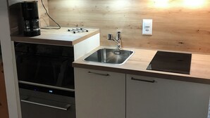 A compact kitchen with a built-in oven, a coffee maker, a sink, and a stove. - Apartment in Täsch / Zermatt for two persons (Täsch)