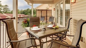 Eine überdachte Terrasse mit Tisch für zwei Personen, Gartenstühlen und einem Deckenventilator.