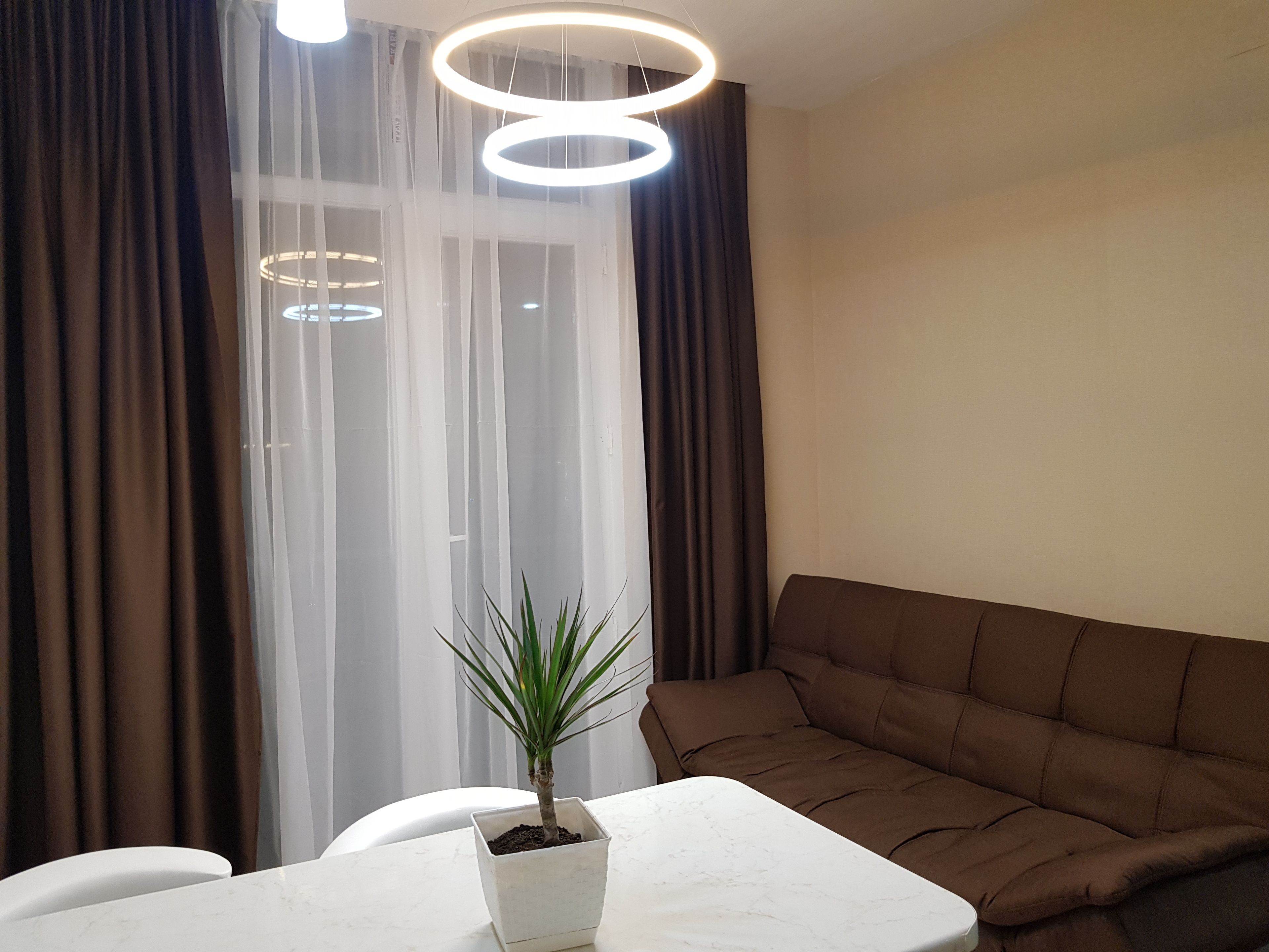 A modern living room with a white table, a brown sofa, and a potted plant.