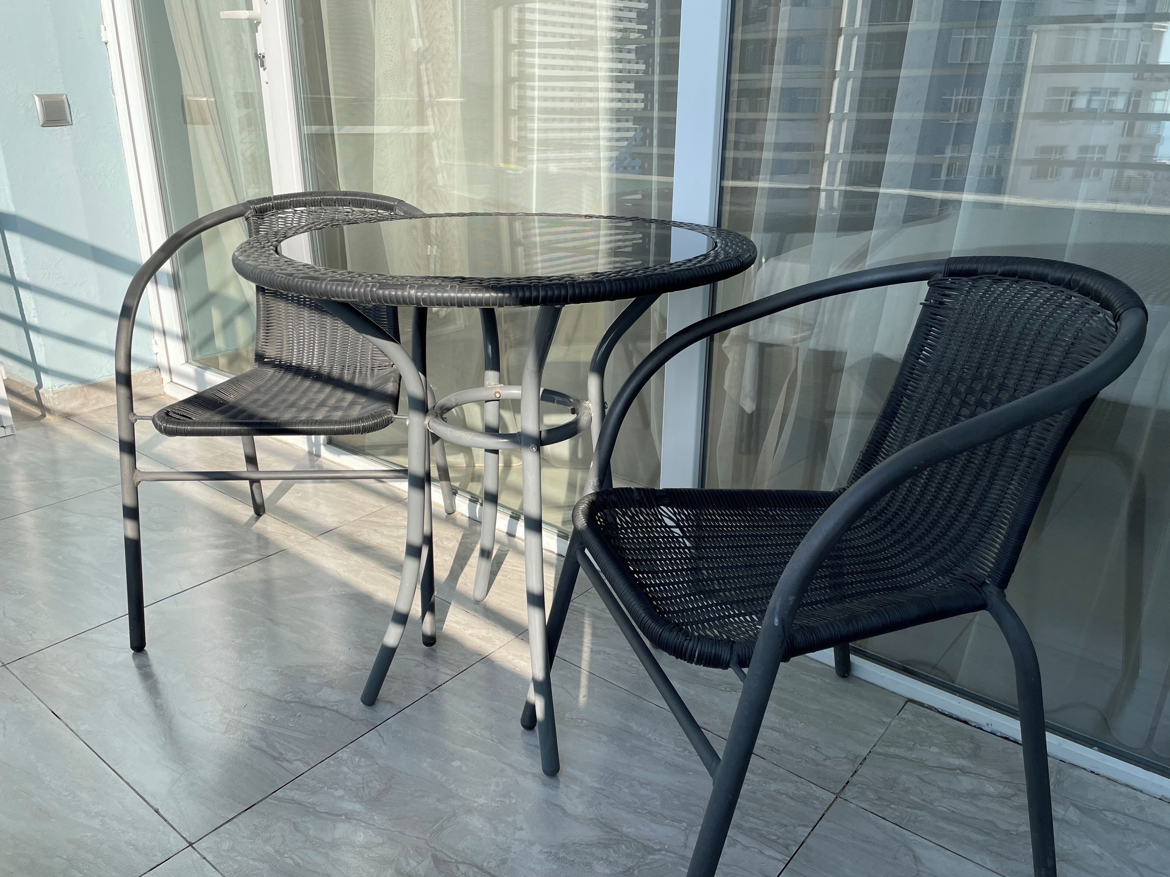 A balcony with a glass table and two wicker chairs.
