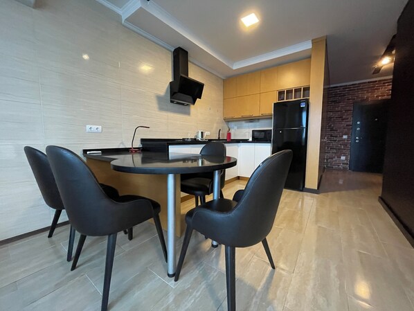 A modern kitchen with a round dining table, black chairs, and a built-in stove. - Batumi Real Lux (Batumi)
