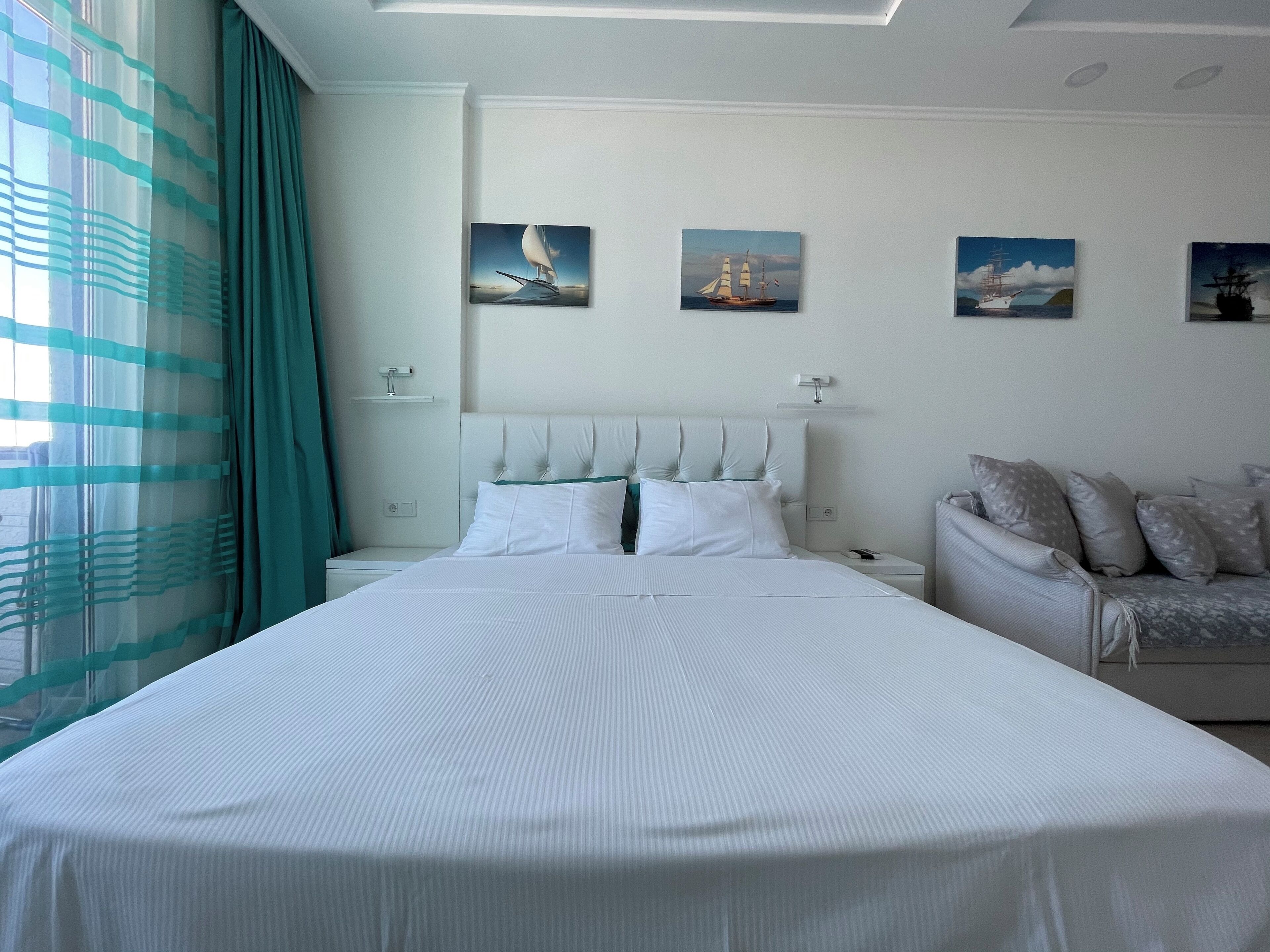 Une chambre d’hôtel moderne, dotée d’un grand lit, d’un canapé et offrant une vue sur la mer par la fenêtre.