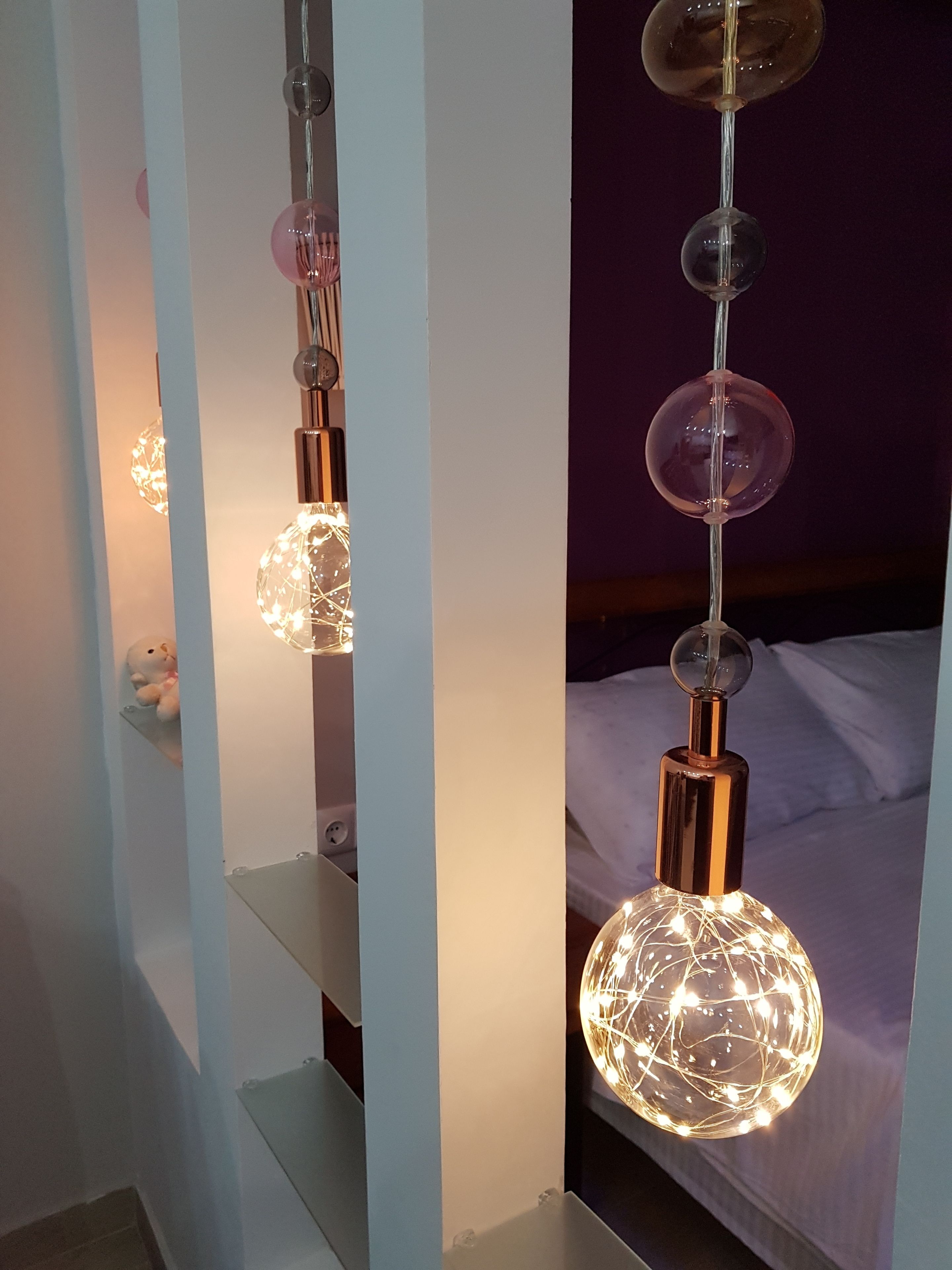 A room with a bed, a nightstand, and a hanging light fixture with spherical glass bulbs.