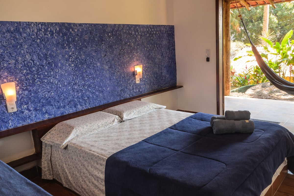 A bedroom with a large bed, a hammock, and a view of greenery outside.
