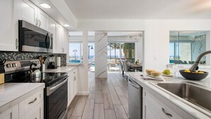 A modern kitchen with white cabinetry, a black stove, and a large island with a sink. - Ocean-view 5BR with private pool (Fort Lauderdale)