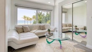 A modern living room with a large glass coffee table, a white leather sofa, and a view of the beach. - Ocean-view 5BR with private pool (Fort Lauderdale)