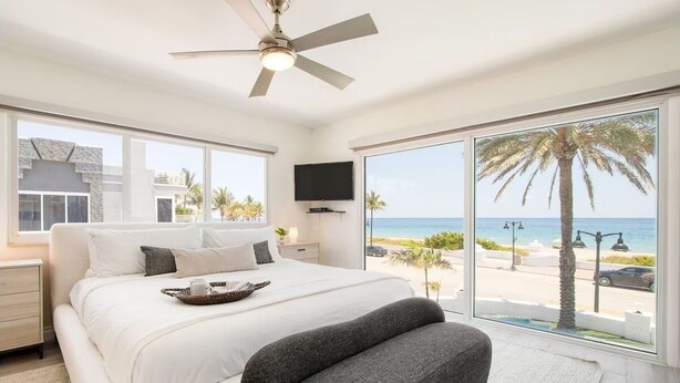 A bedroom with a large bed, a ceiling fan, a TV, and a view of the beach. - Ocean-view 5BR with private pool (Fort Lauderdale)