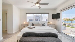 A modern bedroom with a large bed, a ceiling fan, a TV, and a view of the street. - Ocean-view 5BR with private pool (Fort Lauderdale)
