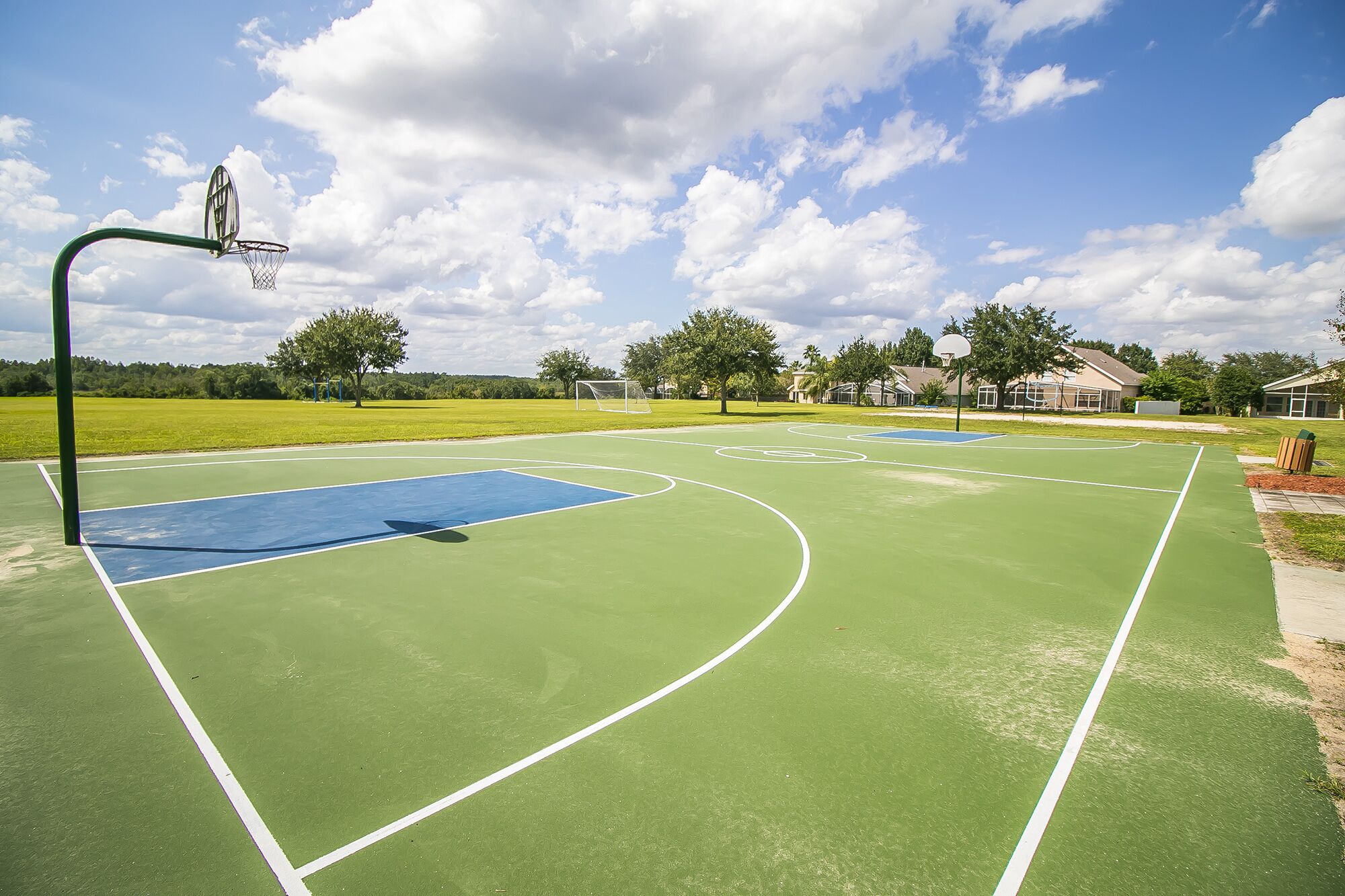 An outdoor basketball court with a green surface, white boundary lines, and a basketball hoop.