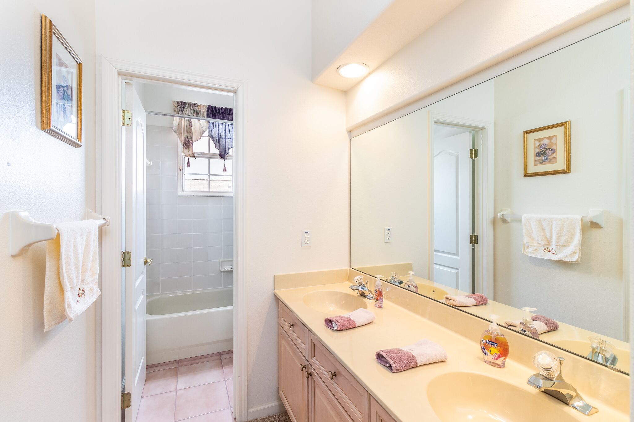 A bathroom with a bathtub, two sinks, a large mirror, and towels on the wall.
