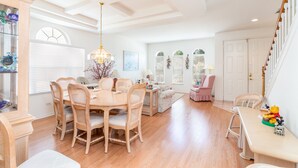 A spacious living room with a wooden dining table and chairs, a sofa, and a staircase with a railing. - SEASONAL LOW RATES!!!Located in Disney's backyard- WITH PRIVATE POOL!!! (Clermont)