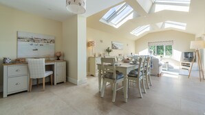 A spacious dining area with a high ceiling and skylights, a kitchen with modern appliances, and a cozy seating area with a television.