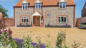 A two-story house with a stone facade, a tiled roof, and a front garden with gravel and purple flowers.