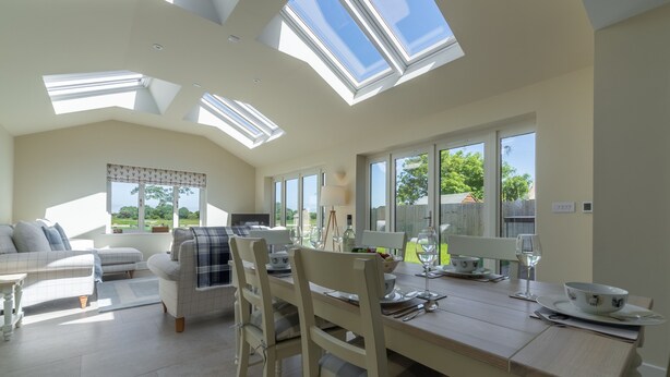 A spacious living area with a high ceiling, skylights, a dining table set for four, and a comfortable seating arrangement.