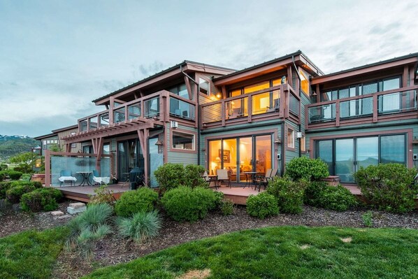 A modern multi-story house with a glass facade, outdoor seating area, and landscaped garden.