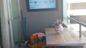 A balcony with a table, chairs, a vase with flowers, a painting, and a window overlooking a building. - There's still time to make your reservation for Carnival, excellent apartment, take advantage! (Cabo Frio)